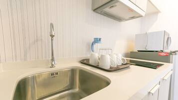 Una cocina moderna con un lavamanos de acero inoxidable, armarios blancos y una cafetera en la encimera.