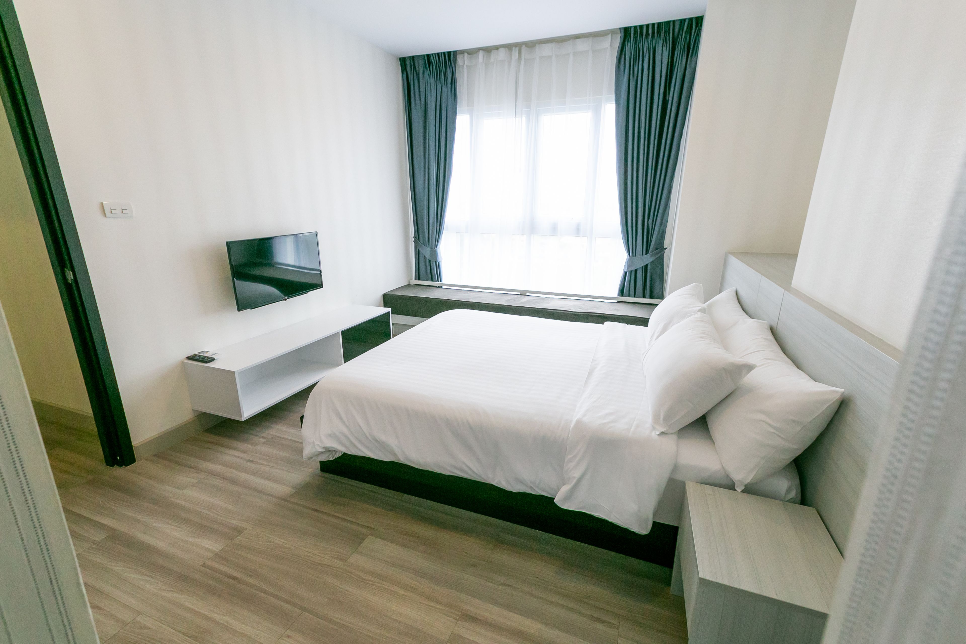A modern hotel room with a large bed, a TV on a stand, and a window with curtains.