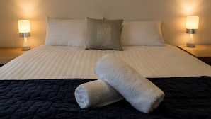 Una cama bien hecha con ropa de cama a rayas, dos almohadas y dos lámparas de noche.