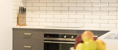 A kitchen with white tiled backsplash, stainless steel appliances, and a fruit bowl on the counter.