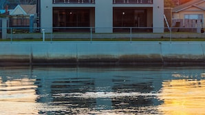 Un edificio moderno de dos pisos con ventanas amplias y un balcón, cerca de una masa de agua.