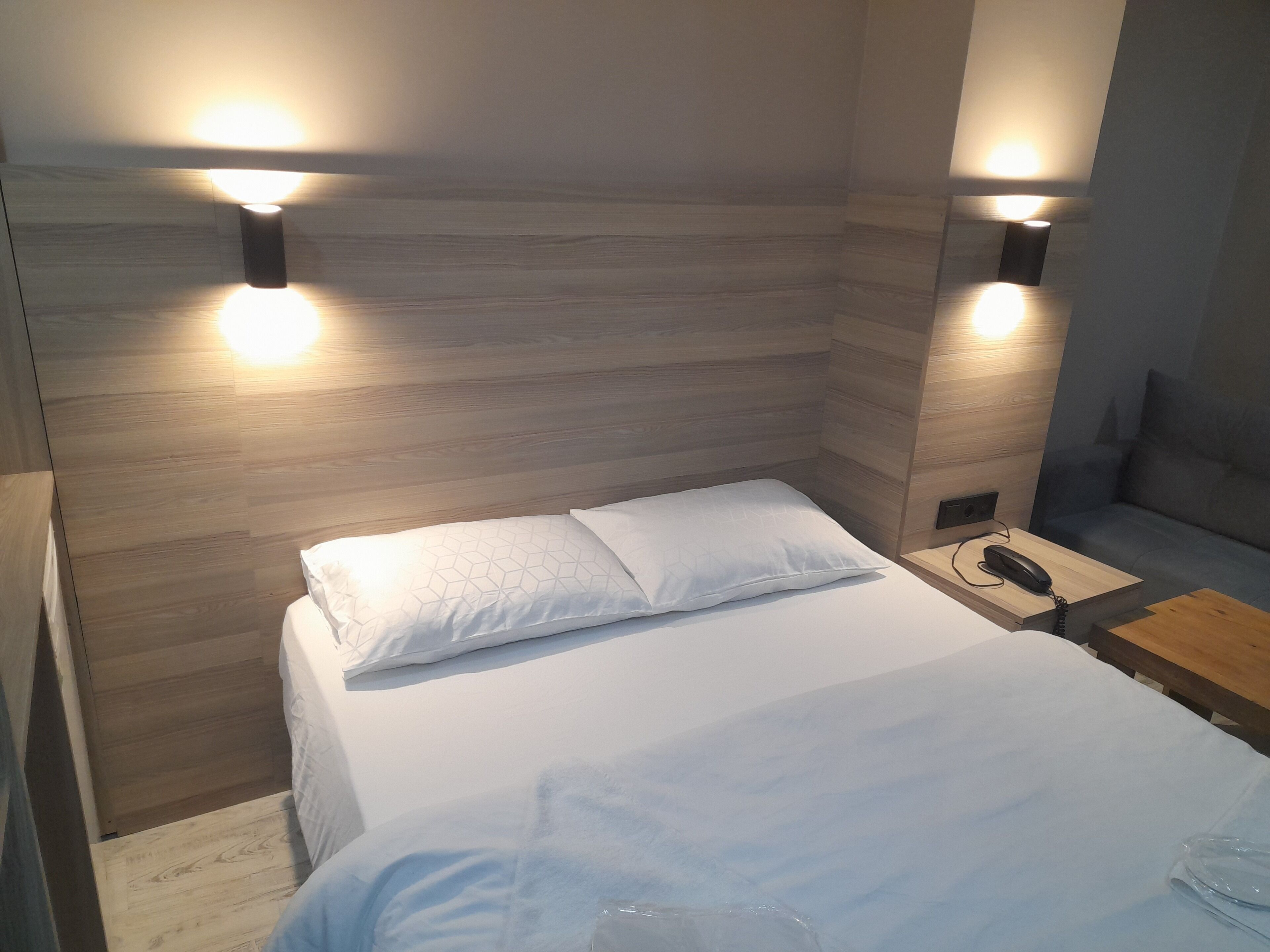 A modern bedroom with a wooden headboard, a bed with white linens, and bedside lamps.