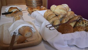 A variety of breads and pastries on a table, including a loaf of bread on a cutting board and a basket of rolls. - Luisenstuben (Badenweiler)