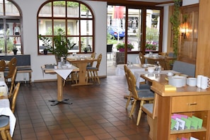 A restaurant with wooden tables and chairs, large windows with plants, and a tiled floor. - Luisenstuben (Badenweiler)
