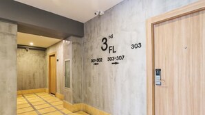 A hallway with a tiled floor, a wooden door, and a wall with room numbers and arrows indicating directions. - Happy Bou Jomtien Guesthouse (Pattaya)
