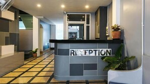 A reception area with a tiled floor, a reception desk, and potted plants. - Happy Bou Jomtien Guesthouse (Pattaya)