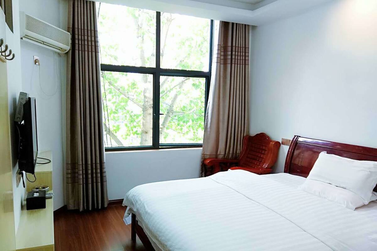 A hotel room with a large bed, a TV, and a window with curtains.