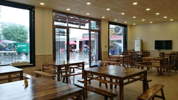 A spacious indoor dining area with wooden tables and benches, large windows, and a ceiling with recessed lighting. - DONG JIANG HU XIANG CUN DA WAN CAI Hotel (Chenzhou)