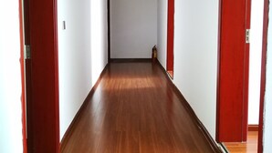 A hallway with wooden flooring and red doors, leading to a room with a white ceiling and a visible fire extinguisher. - DONG JIANG HU XIANG CUN DA WAN CAI Hotel (Chenzhou)