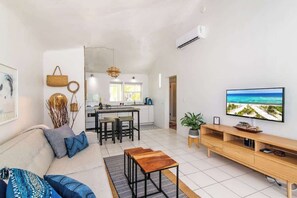 Ein modernes Wohnzimmer mit einer Couch, einem Couchtisch, einem Fernseher und einer Küche im Hintergrund.