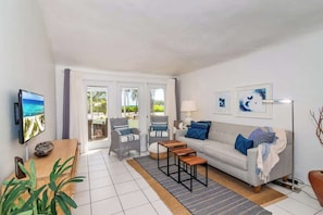Ein modernes Wohnzimmer mit Sofa, Couchtisch und Fernseher. Ein Fenster mit Vorhängen, eine Pflanze und eine Lampe sind ebenfalls vorhanden.
