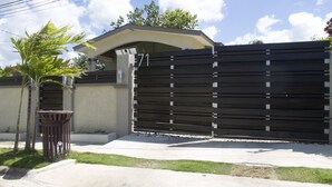 A gated residential area with a concrete driveway, a trash bin, and a palm tree. - Your Home Away from Home (Montego Bay)