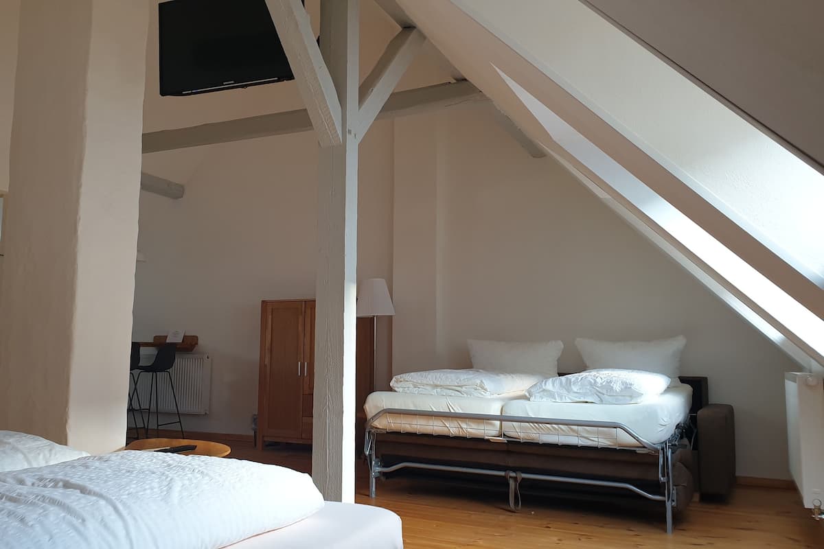 A bedroom with a sloped ceiling, a bed, a wooden wardrobe, and a mirror.