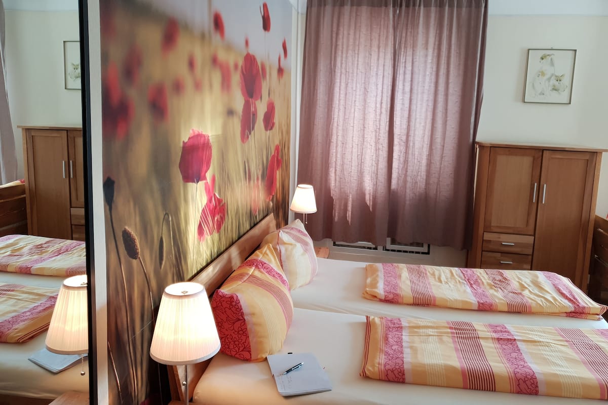 A hotel room with two beds, a large mirror, a lamp, a window with curtains, and a painting on the wall.