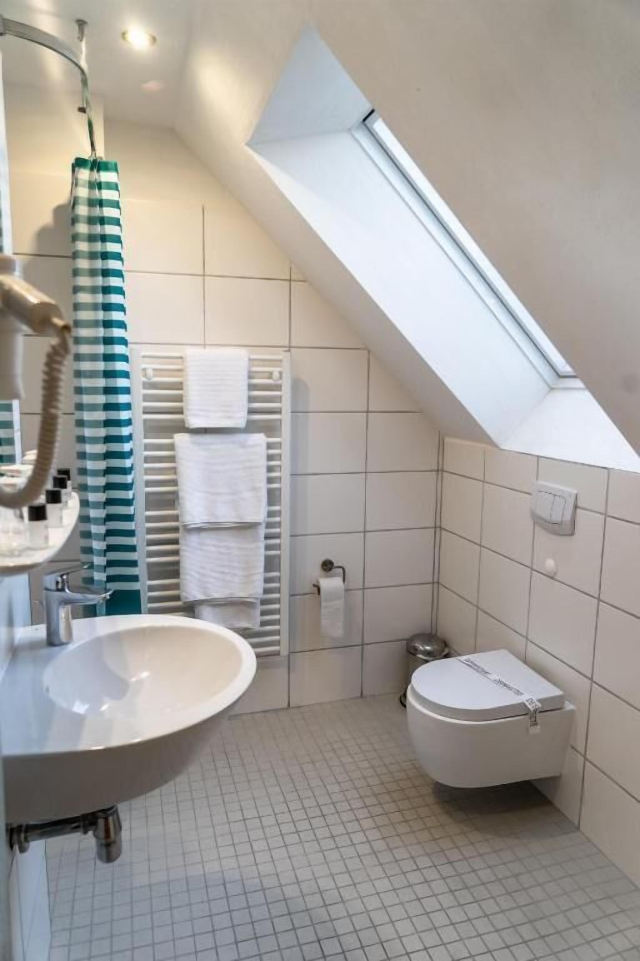 A bathroom with a skylight, a sink, a toilet, and a towel rack.