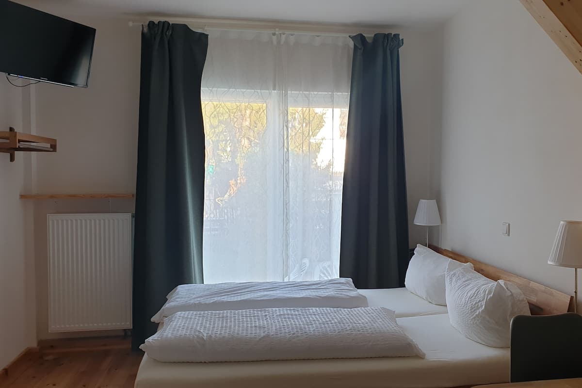 A bedroom with a bed, a TV mounted on the wall, and a window with curtains.