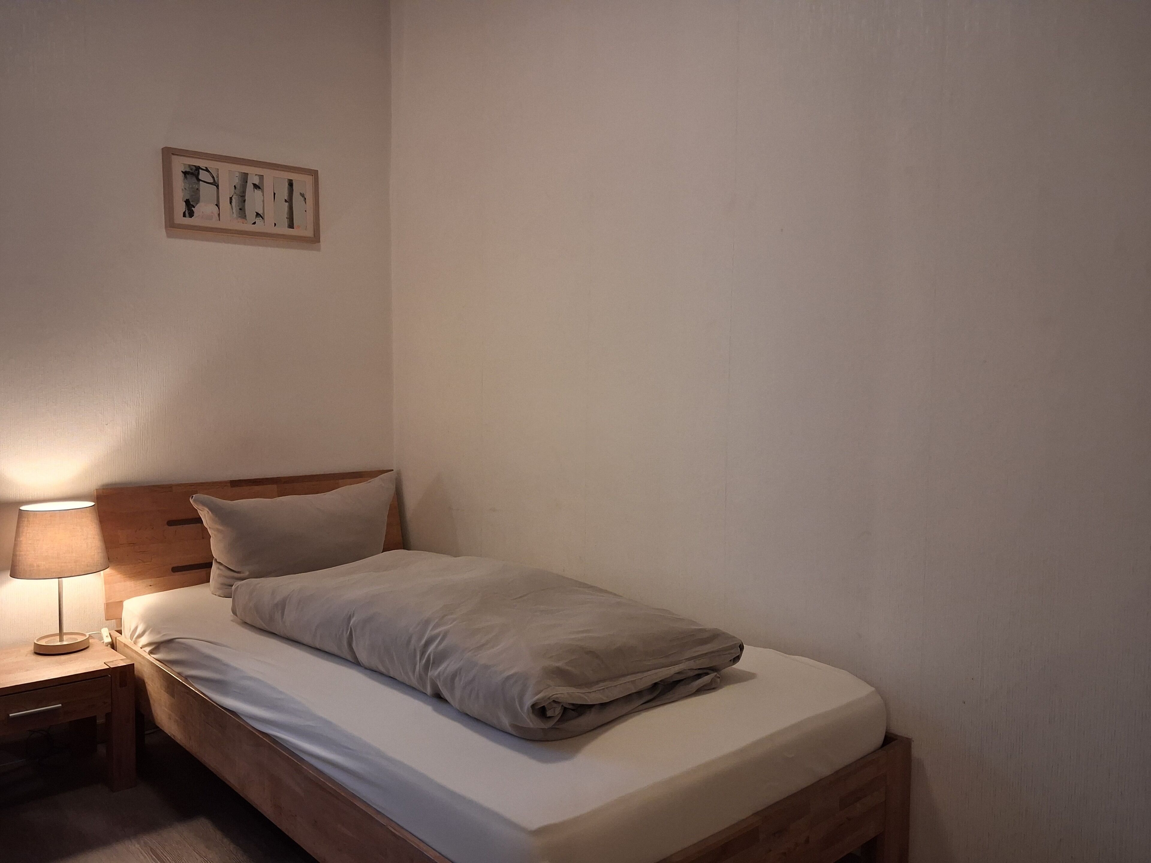 Una cama bien hecha con cabecera de madera, una mesita de noche con una lámpara y un cuadro enmarcado en la pared.