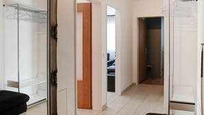 Quarto de hotel com um espelho grande, sofá preto, guarda-roupa e closet espaçoso.