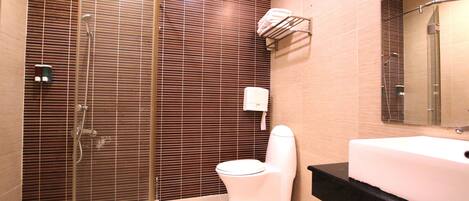 A bathroom with a glass shower enclosure, a white toilet, and a large sink with a black countertop.