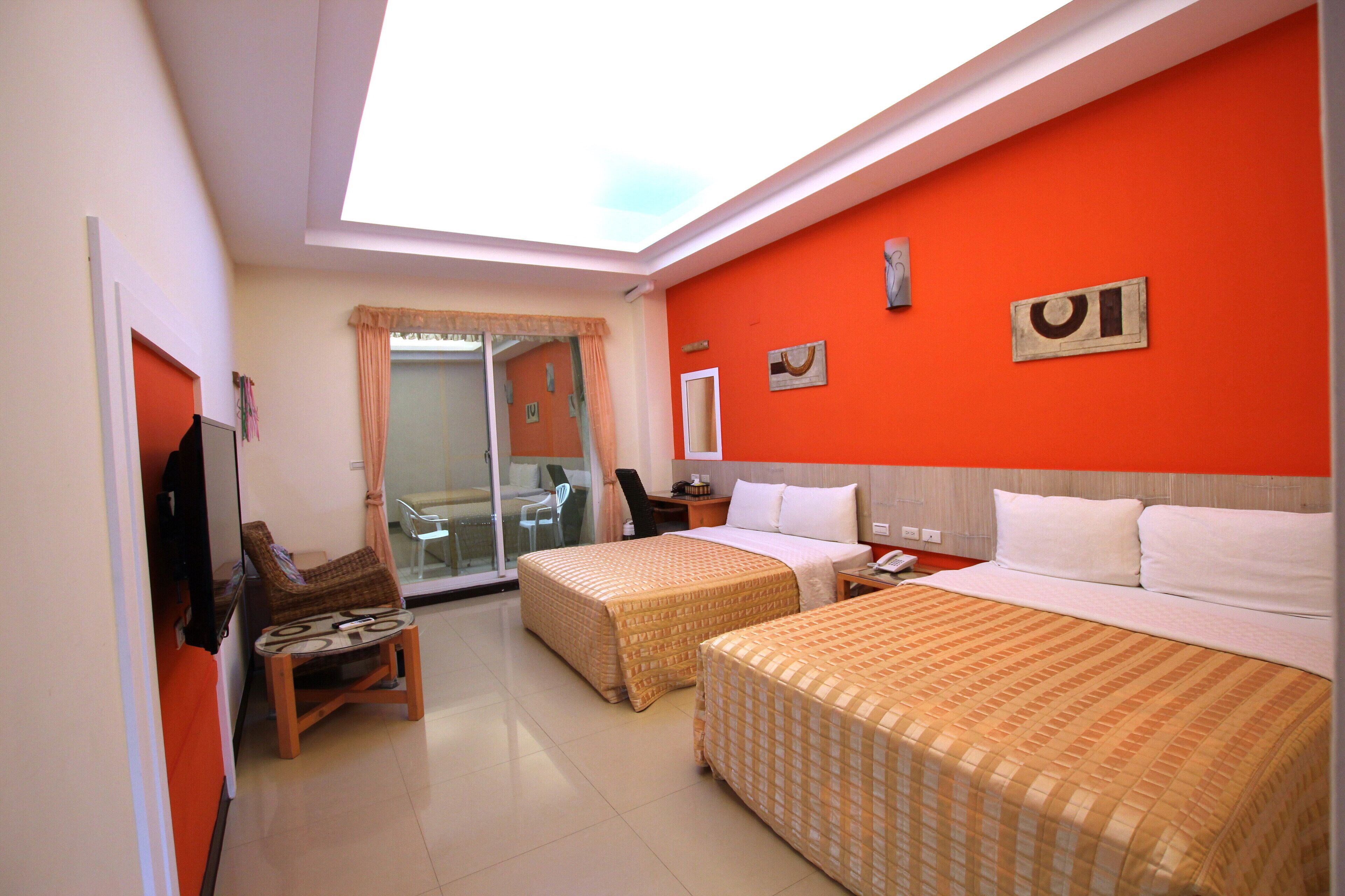 A hotel room with two beds, a TV, a desk, and a view of the street.