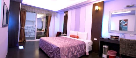 Quarto de hotel moderno com uma cama grande, uma pequena escrivaninha, um espelho e uma porta de correr para uma varanda.