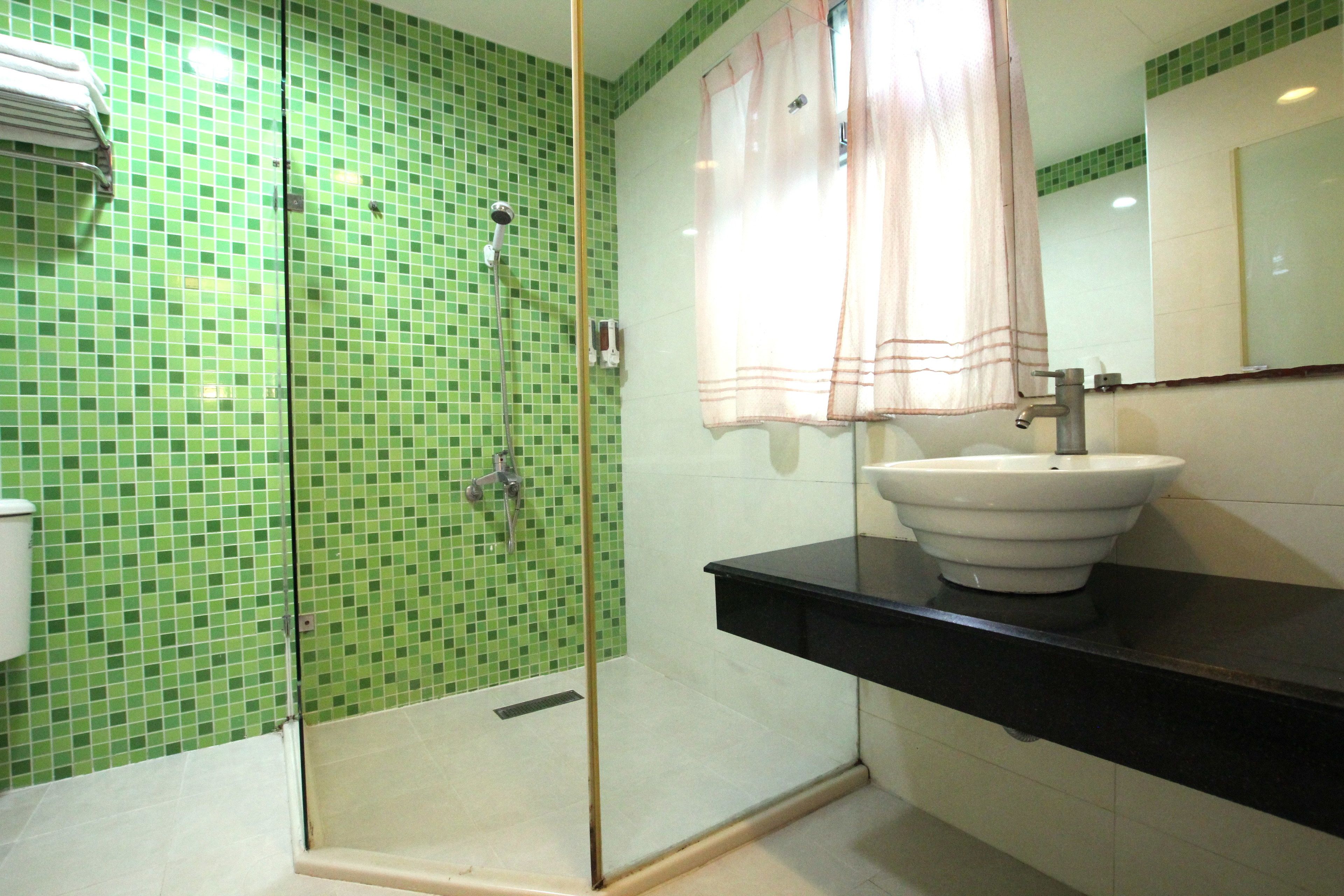 A bathroom with a green mosaic tile wall, a glass-enclosed shower, a white sink, and a black countertop.