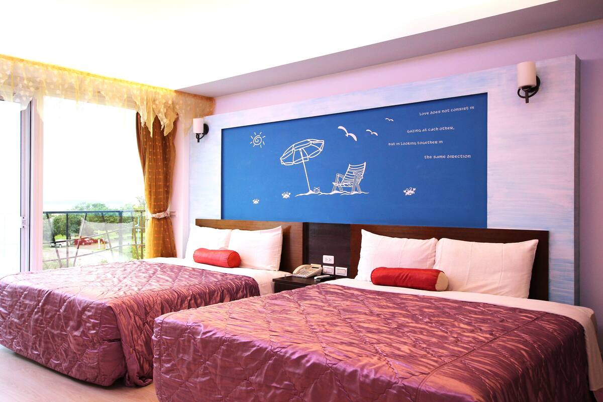 A hotel room with two beds, a balcony, a large wall mural, and a view of the outdoors.