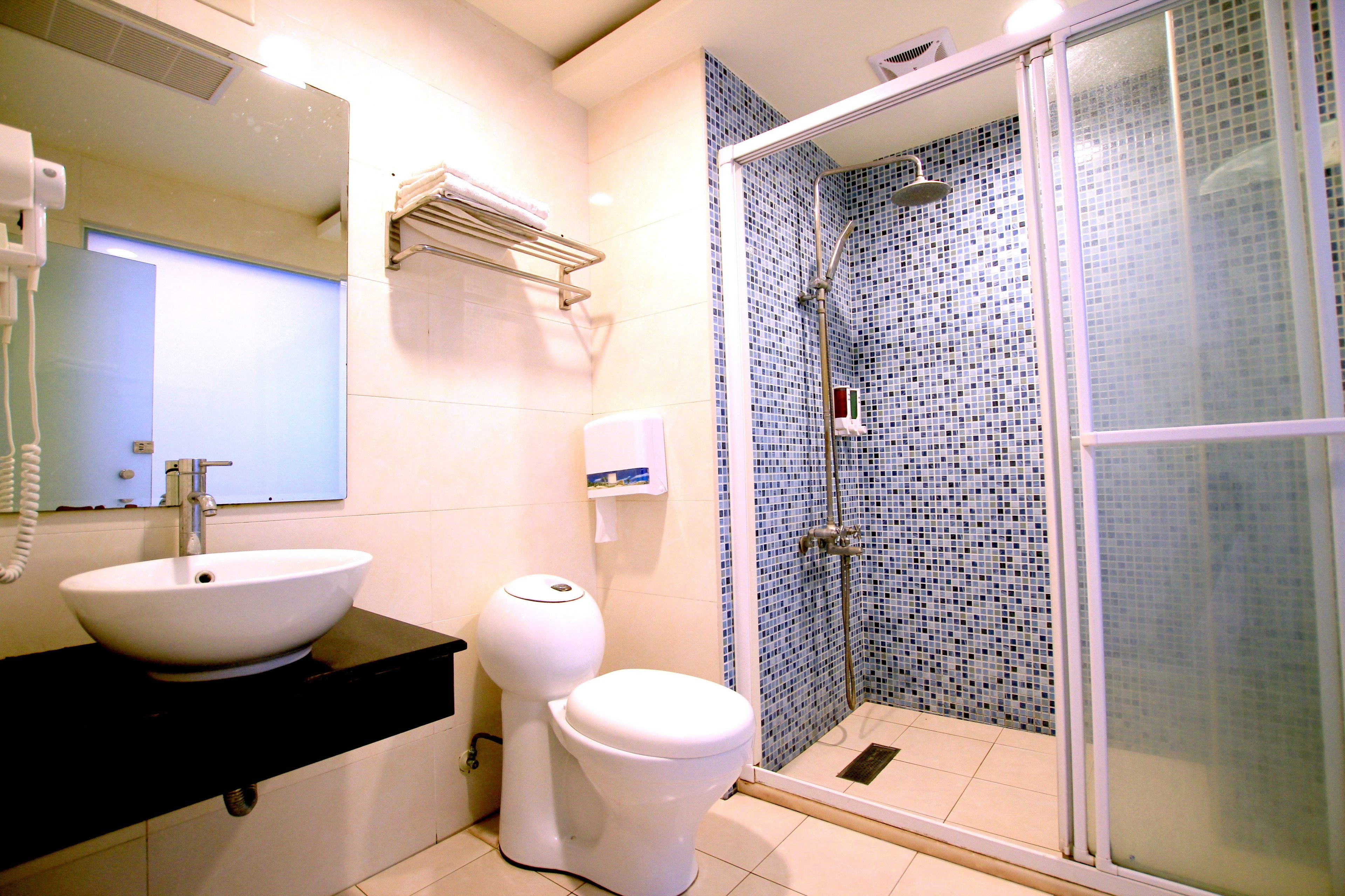 Un baño con lavamanos blanco, inodoro y ducha con mosaicos azules.