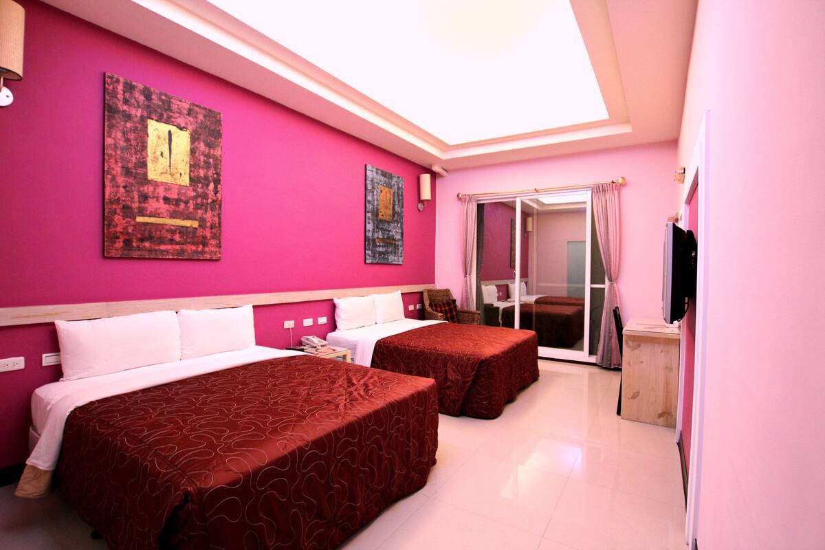 A hotel room with two beds, a large window, and a sliding door leading to a balcony.