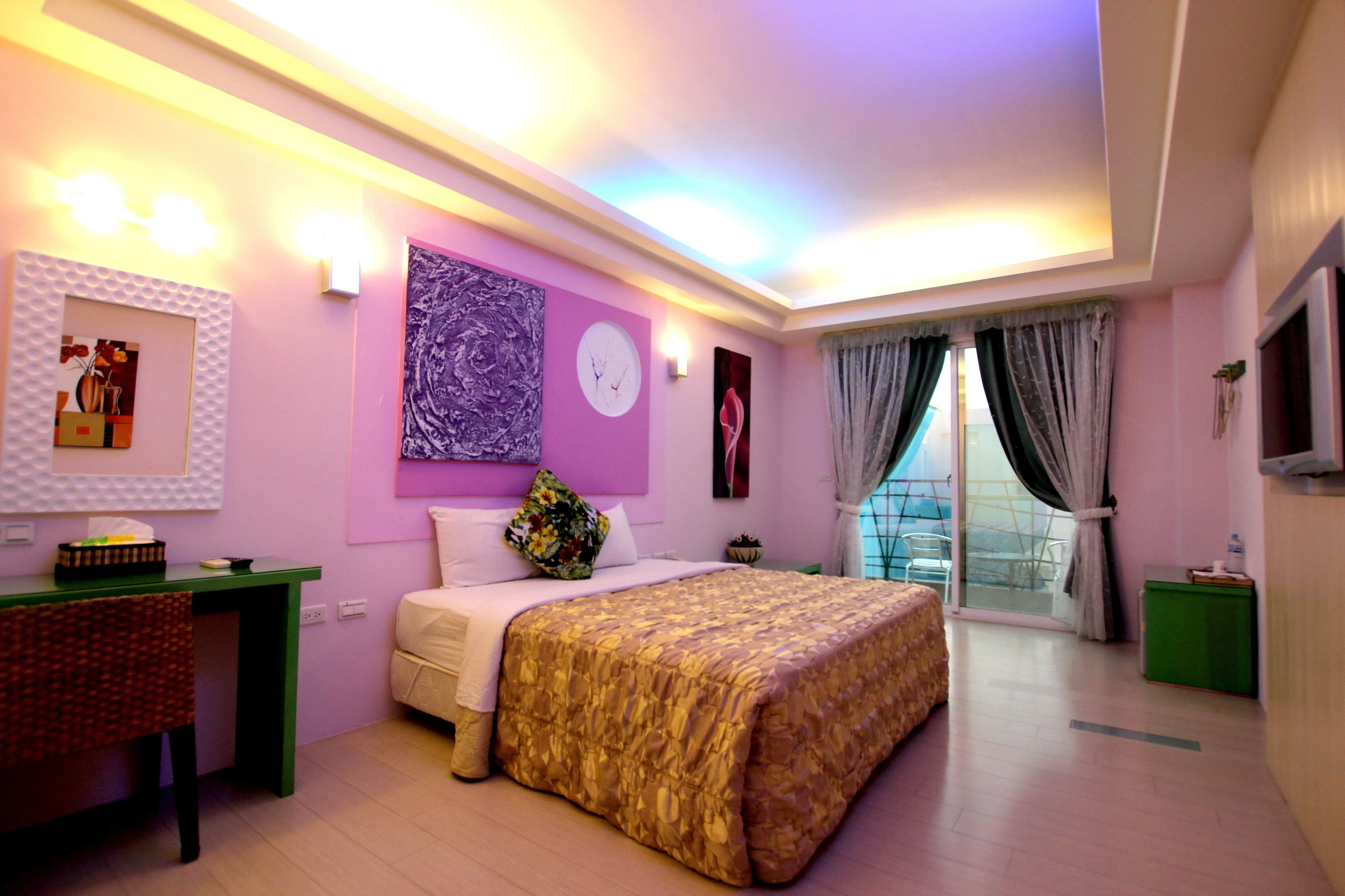 Quarto com cama, escrivaninha, cadeira, televisão e janela com cortinas.
