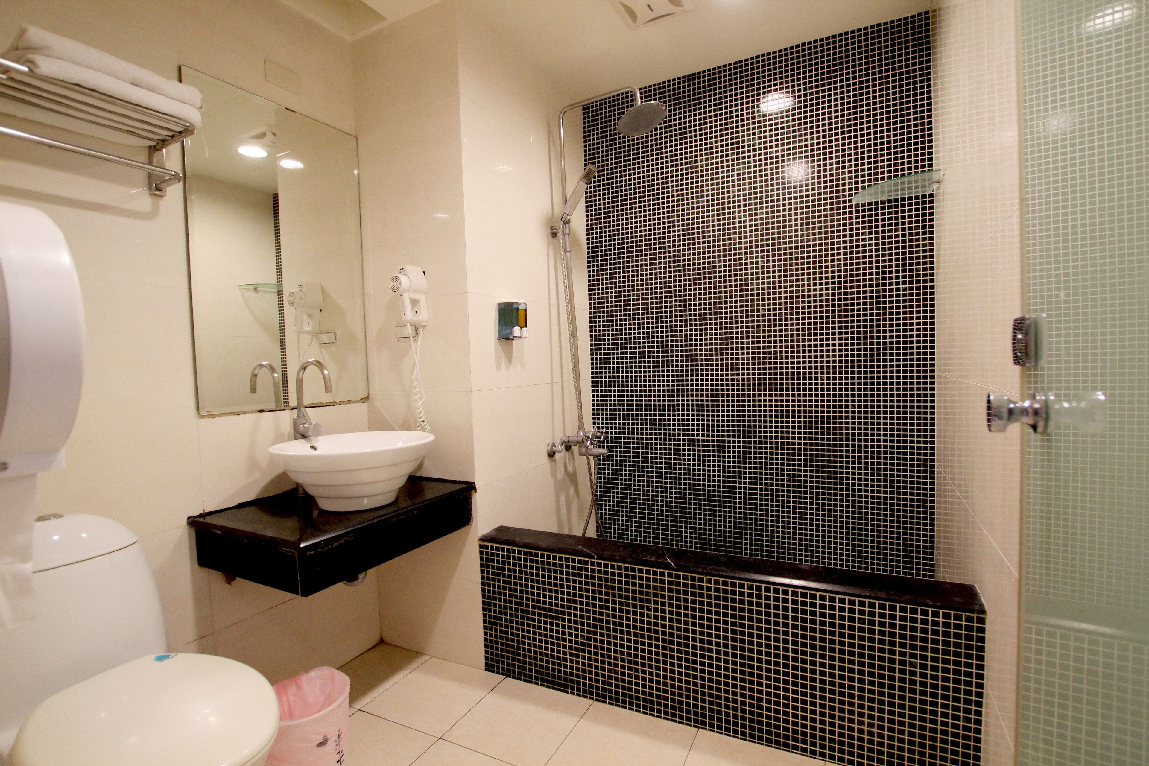 A bathroom with a white toilet, a black sink, a mirror, and a shower area with black tiled walls.
