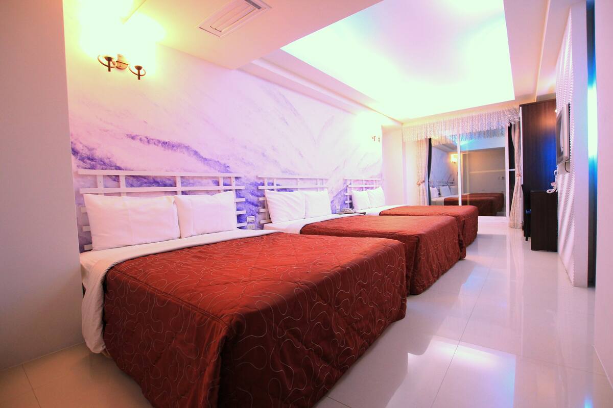A hotel room with three beds, a marble wall, and a bright ceiling light.
