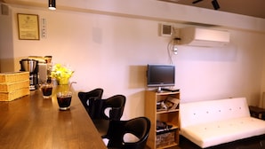 A modern living room with a sofa, a television, a dining table with chairs, and a kitchen area with a microwave and a coffee machine. - SAPPORO GUEST HOUSE NARIYA - Hostel (Sapporo)