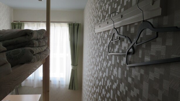 A dormitory room with bunk beds, a wall-mounted coat rack, and a patterned wallpaper. - SAPPORO GUEST HOUSE NARIYA - Hostel (Sapporo)