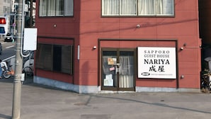 A red multi-story building with a sign for "Sapporo Guest House Nariya" on the ground floor. - SAPPORO GUEST HOUSE NARIYA - Hostel (Sapporo)