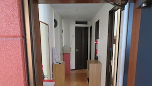 A narrow hallway with a wooden floor, a red bulletin board, and a whiteboard on the left. - SAPPORO GUEST HOUSE NARIYA - Hostel (Sapporo)