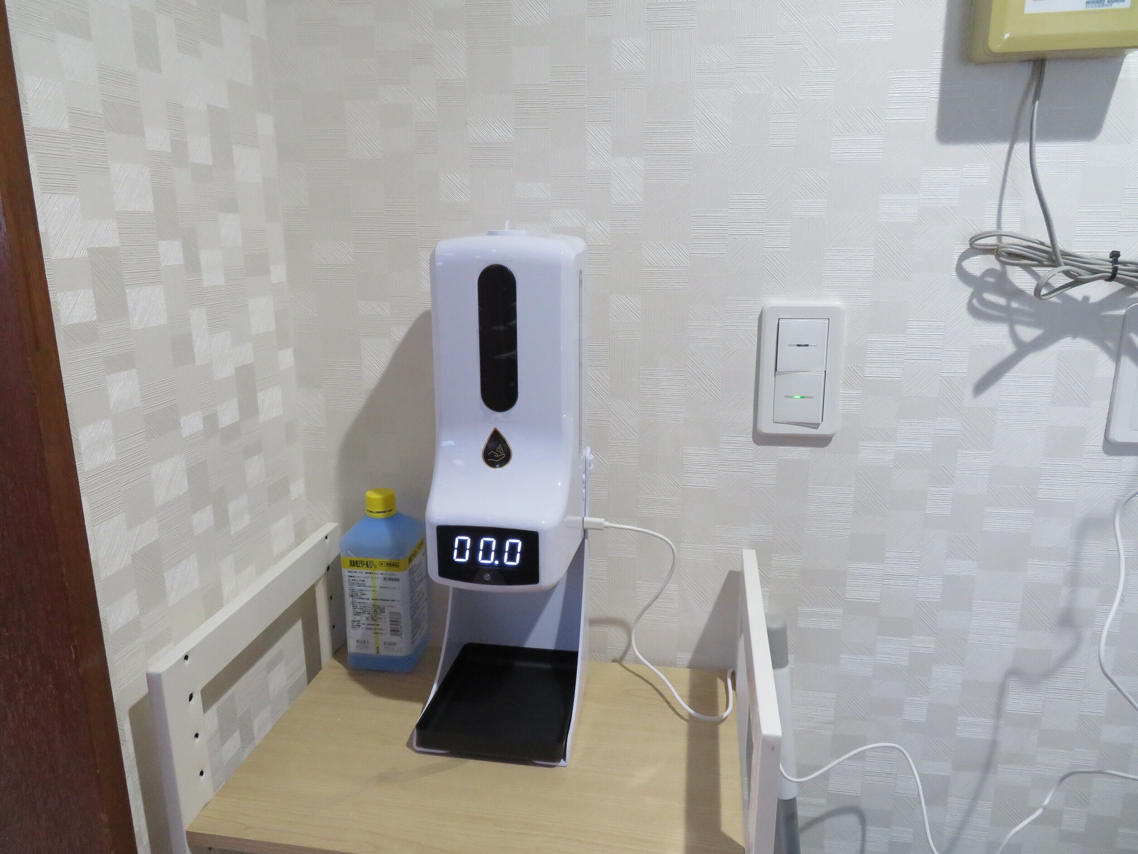 Un distributeur de gel hydroalcoolique doté d’un écran numérique, une bouteille de gel hydroalcoolique et une prise électrique sur un mur.