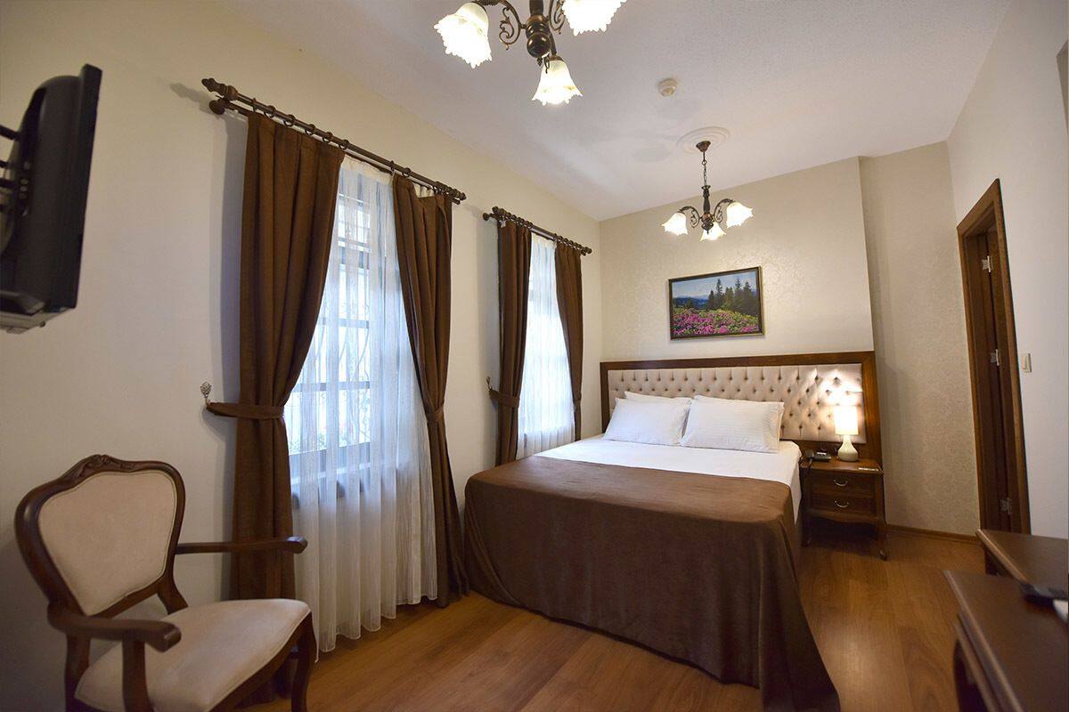 A hotel room with a large bed, a wooden chair, a television, and a painting on the wall.