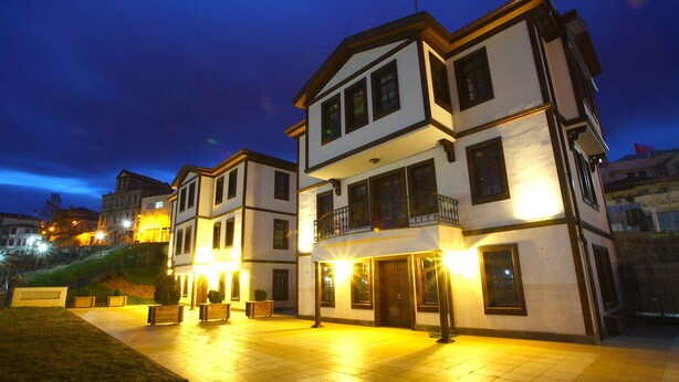 A multi-story building with a balcony on the second floor, a well-lit entrance, and a paved courtyard. - Zagnospasa Konaklari (Trabzon)