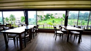 A restaurant with wooden tables and chairs, large windows offering a view of a green park and buildings. - Zagnospasa Konaklari (Trabzon)