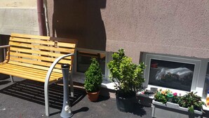 Una cadira de fusta, dues plantes en testos i una finestra amb vista a un edifici.