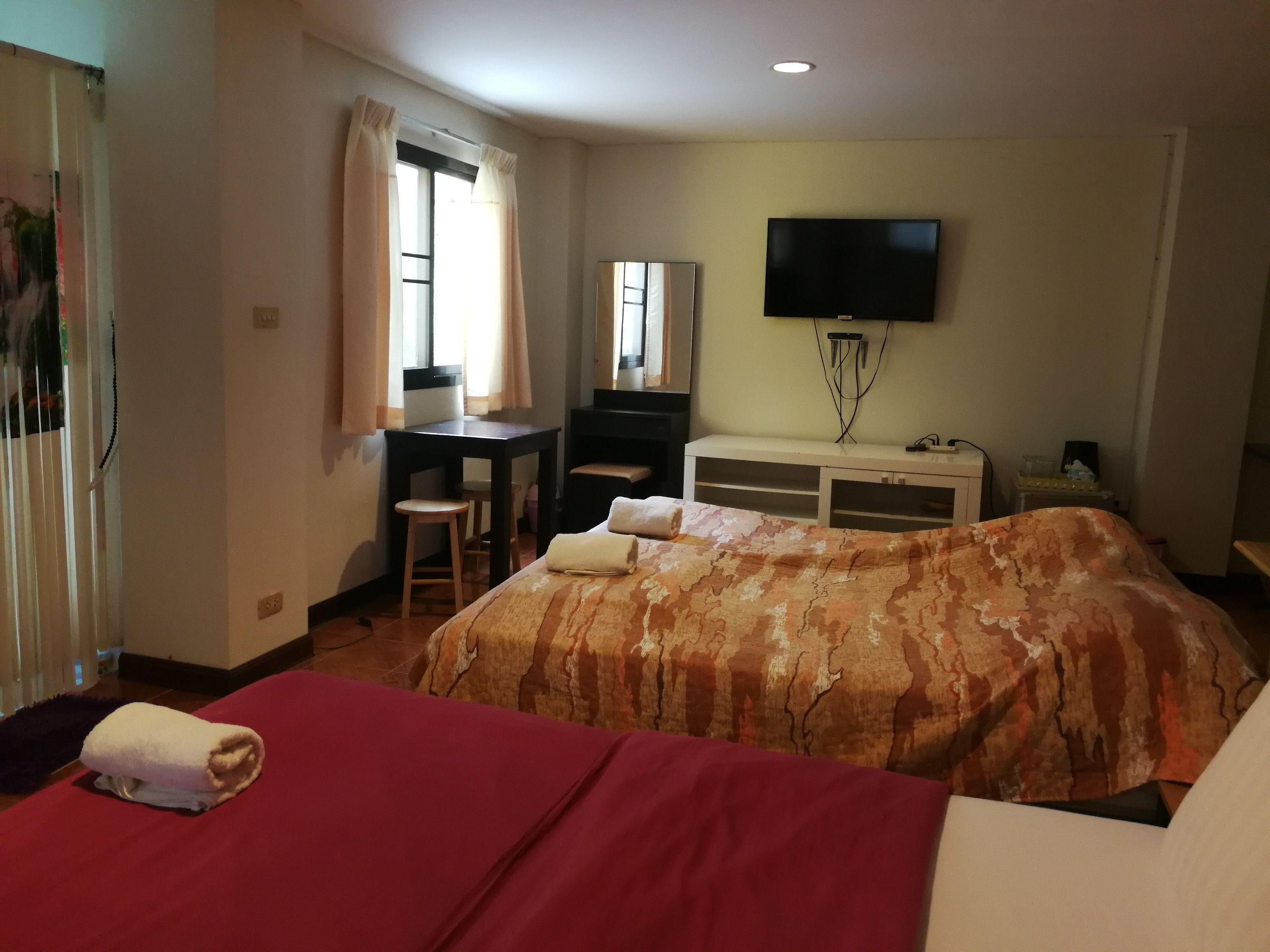 A hotel room with two beds, a desk, a chair, a TV, and a window with curtains.