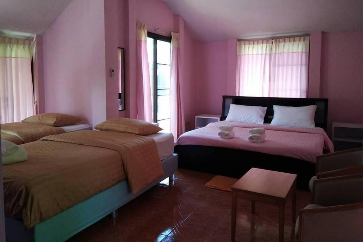A hotel room with a large bed, two smaller beds, a bedside table, and a chair.