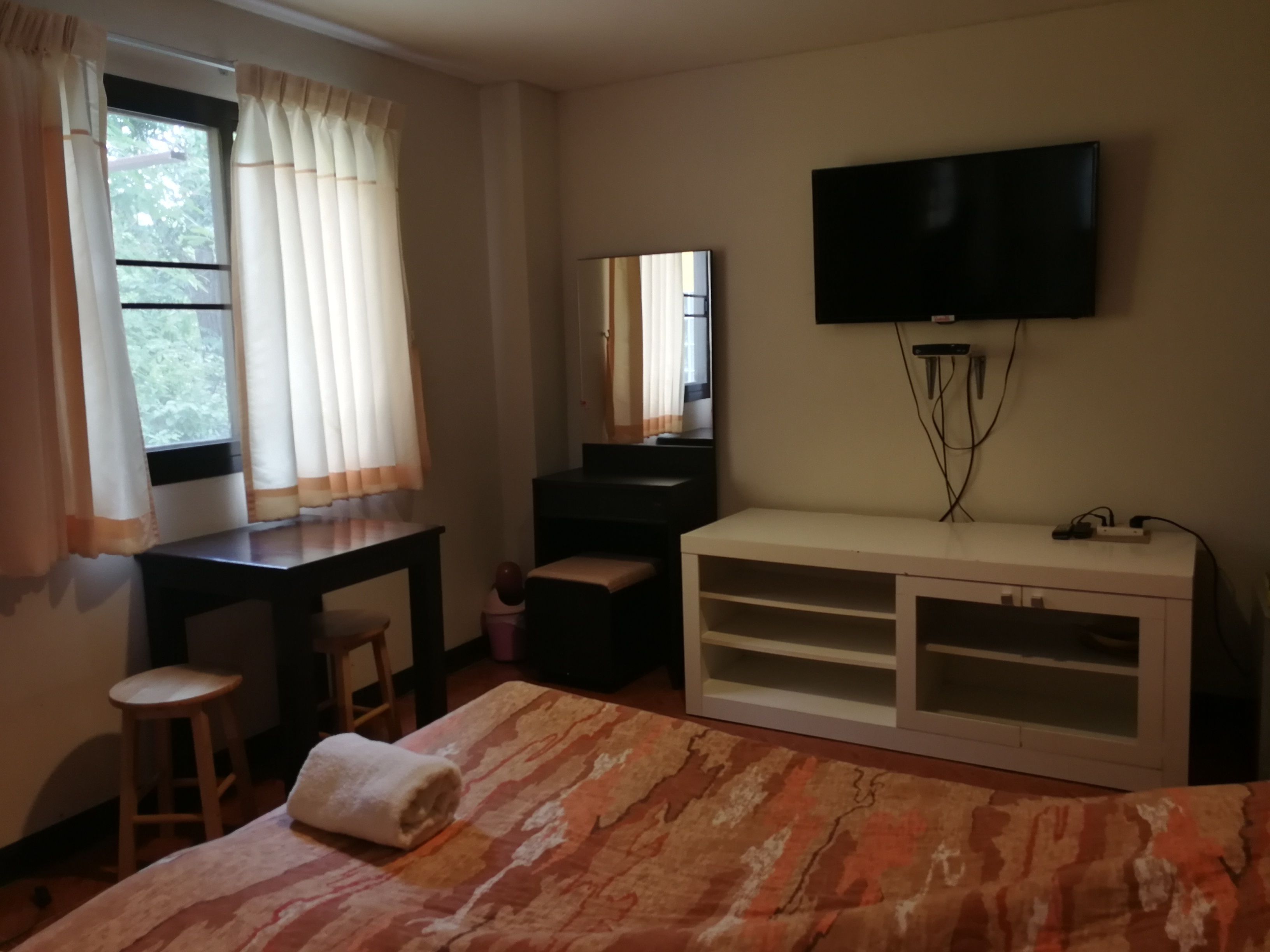 Habitación de hotel con cama, escritorio, silla, televisor y ventana con cortinas.