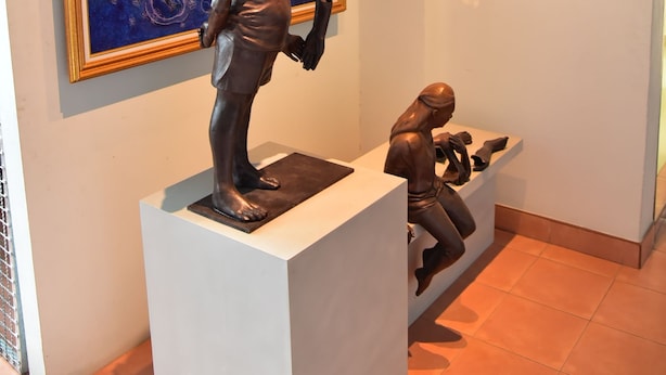 A sculpture of a man holding a child on a pedestal, with a painting and framed pictures on the wall behind. - Mekpufah Apartment (Chonburi)