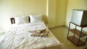 A neatly made bed with a floral duvet, a striped pillow, and a plain pillow. A small wooden shelf with a television is to the right. - Mekpufah Apartment (Chonburi)