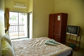 A bedroom with a bed, a wooden wardrobe, a television on a stand, and a balcony with a view. - Mekpufah Apartment (Chonburi)