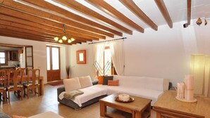 Un ampio soggiorno con soffitto in legno, un divano, un tavolo da pranzo e una cucina visibile tramite una porta aperta.