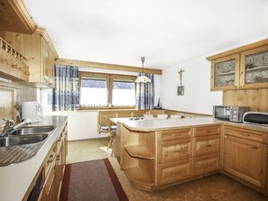 A kitchen with wooden cabinets, a built-in island, a microwave, and a large window with curtains.