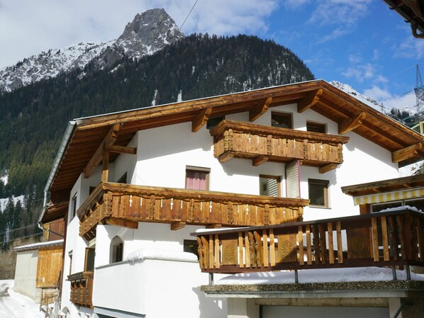 A white building with wooden balconies and a mountain backdrop.